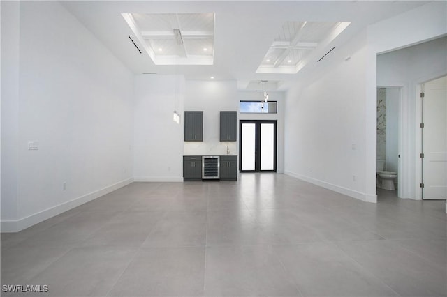 unfurnished room featuring a towering ceiling, beverage cooler, and coffered ceiling