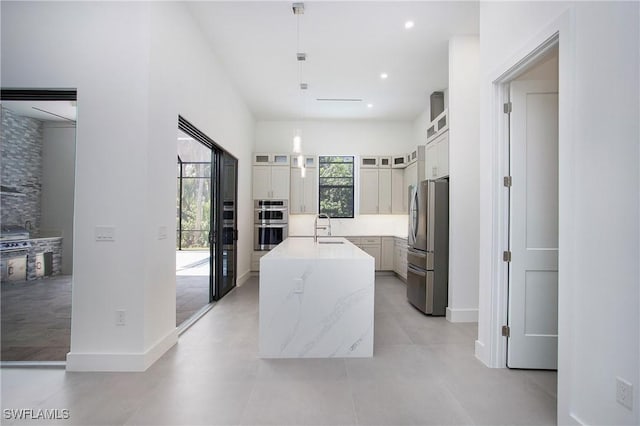 kitchen featuring light stone countertops, appliances with stainless steel finishes, a kitchen island with sink, sink, and decorative light fixtures