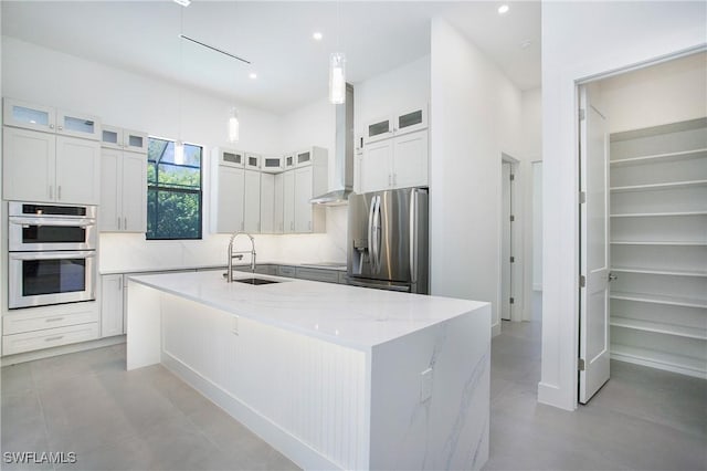 kitchen featuring light stone countertops, stainless steel appliances, sink, decorative light fixtures, and a center island with sink