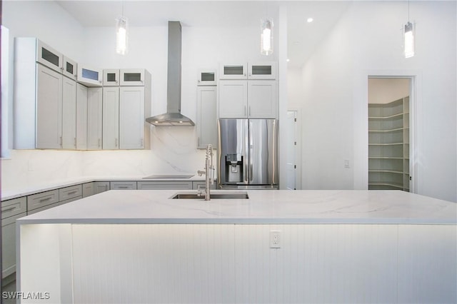 kitchen featuring stainless steel fridge, an island with sink, decorative light fixtures, and wall chimney range hood