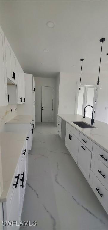 kitchen featuring decorative light fixtures, light stone counters, white cabinetry, and sink