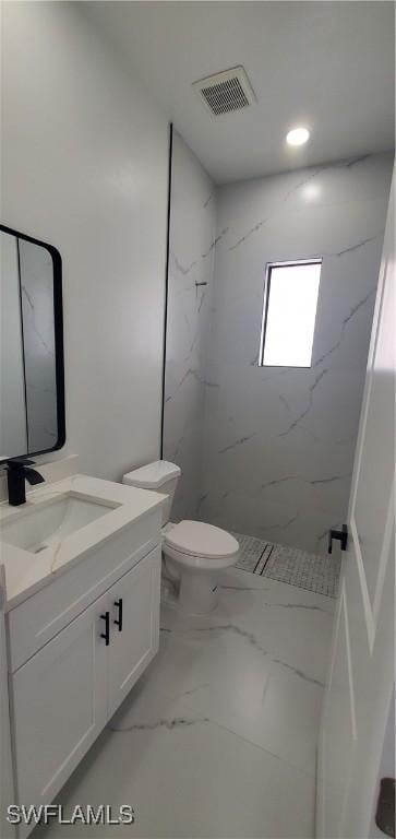 bathroom with a tile shower, vanity, and toilet