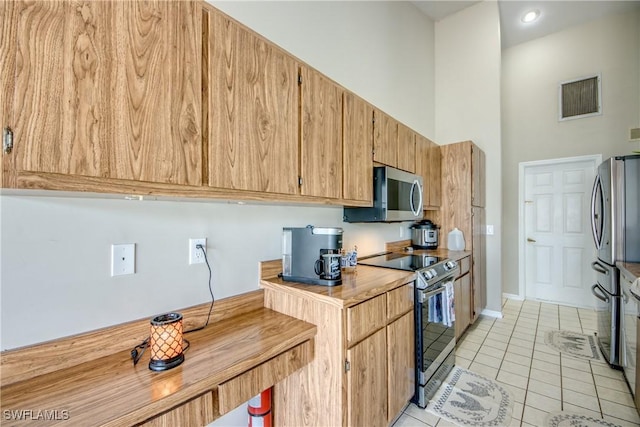 kitchen with light tile patterned floors, stainless steel appliances, and a towering ceiling