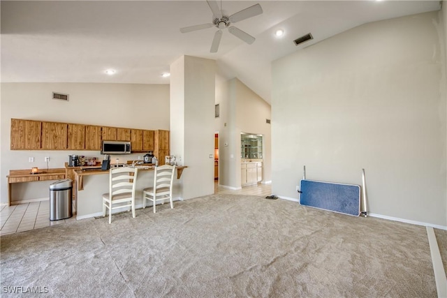 kitchen with ceiling fan, high vaulted ceiling, kitchen peninsula, light colored carpet, and a breakfast bar area