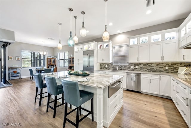 kitchen featuring decorative light fixtures, white cabinets, appliances with stainless steel finishes, and a kitchen island