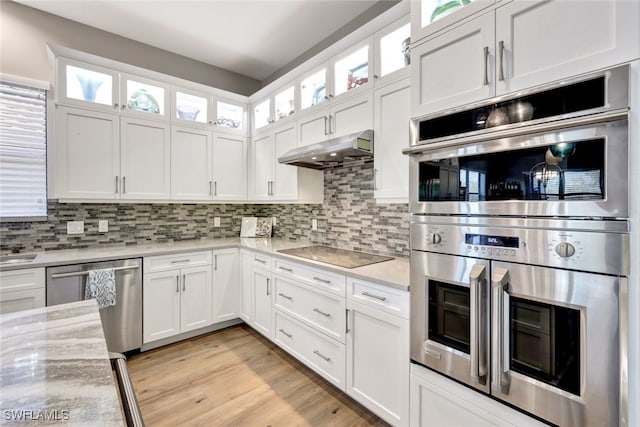 kitchen with appliances with stainless steel finishes, white cabinetry, light hardwood / wood-style floors, backsplash, and light stone counters