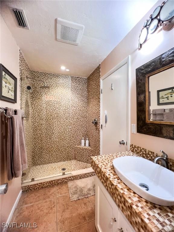 bathroom with tile patterned flooring, vanity, a textured ceiling, and tiled shower