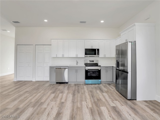 kitchen with light hardwood / wood-style floors, white cabinetry, backsplash, and appliances with stainless steel finishes