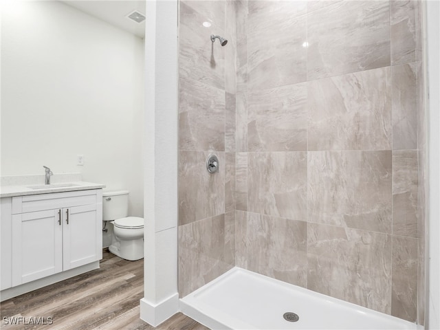 bathroom with tiled shower, hardwood / wood-style floors, vanity, and toilet