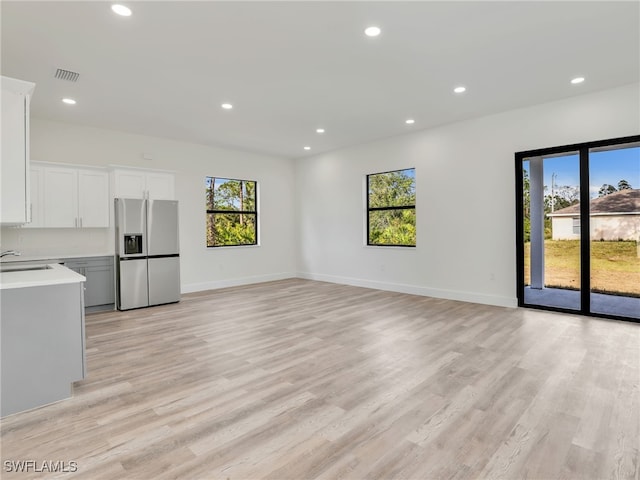 unfurnished living room featuring a wealth of natural light, sink, and light hardwood / wood-style floors