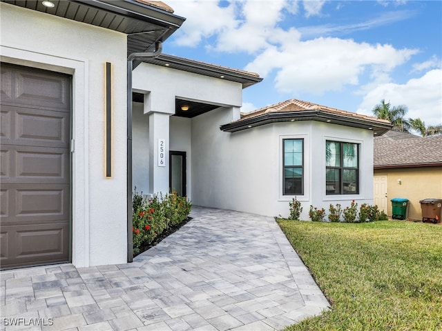 view of exterior entry with stucco siding, a lawn, and an attached garage