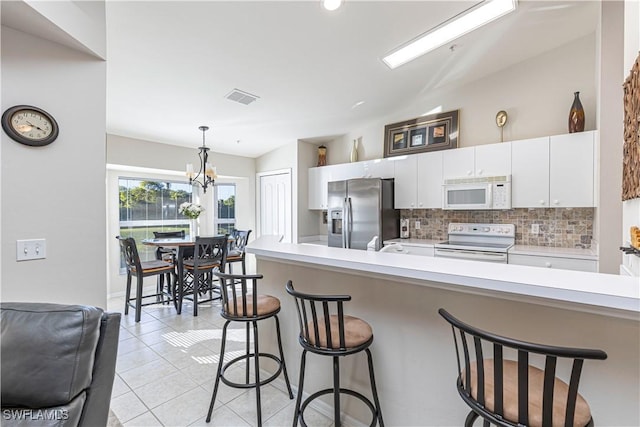 kitchen featuring white appliances, visible vents, decorative backsplash, and a breakfast bar area