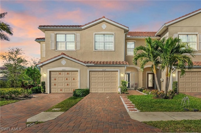view of front of house with a tile roof, a garage, stucco siding, and driveway