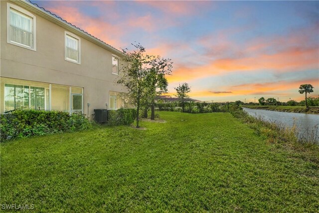 yard at dusk with central AC and a water view