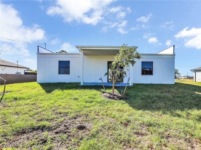 rear view of house featuring stucco siding, a yard, and fence