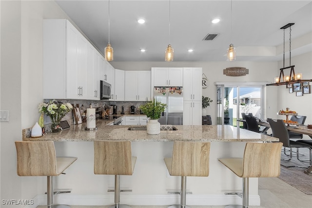 kitchen featuring white cabinetry, a kitchen bar, kitchen peninsula, and stainless steel appliances