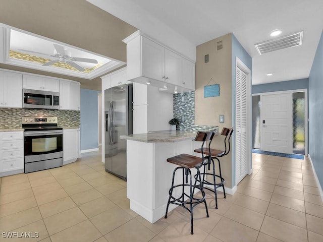 kitchen featuring kitchen peninsula, appliances with stainless steel finishes, backsplash, and white cabinets