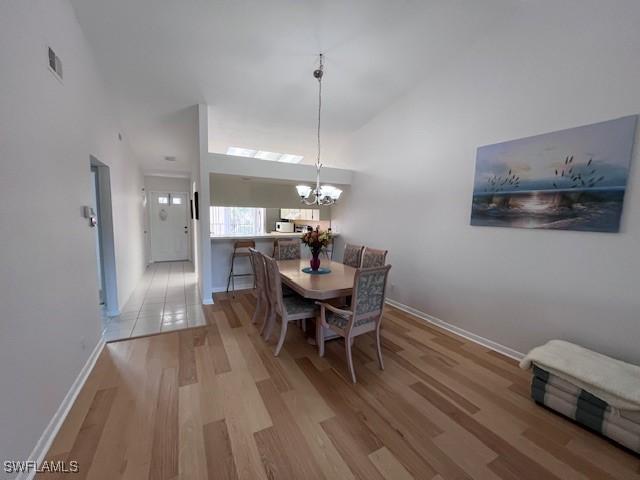 dining room featuring visible vents, a high ceiling, a chandelier, light wood-type flooring, and baseboards