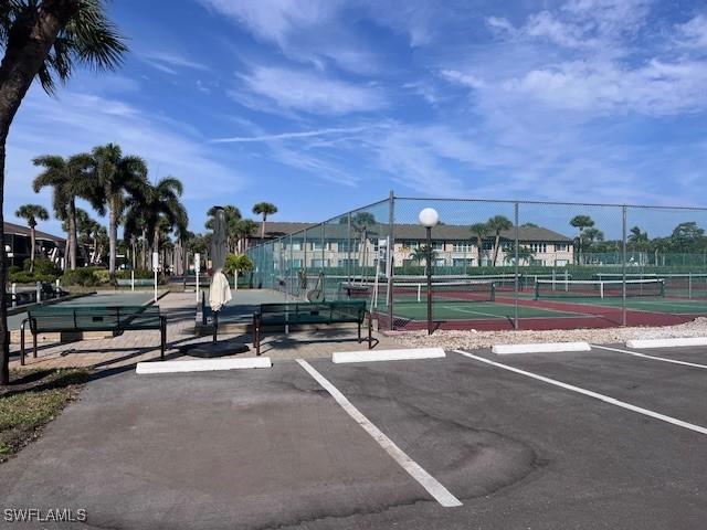 uncovered parking lot featuring a tennis court and fence