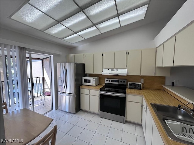 kitchen with lofted ceiling, sink, light tile patterned floors, appliances with stainless steel finishes, and range hood