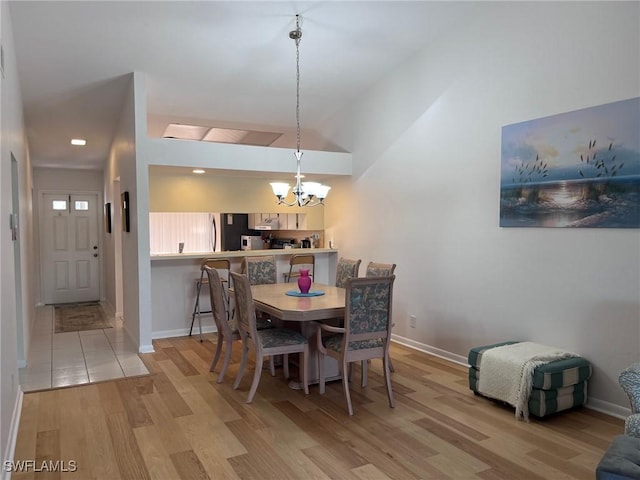 dining space with lofted ceiling, light wood finished floors, baseboards, and a notable chandelier