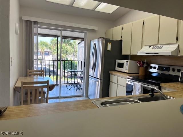 kitchen with stainless steel appliances, light countertops, white cabinetry, a sink, and ventilation hood