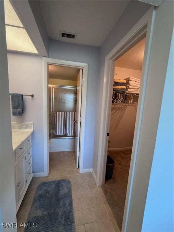 bathroom with tile patterned flooring, vanity, visible vents, baseboards, and a spacious closet