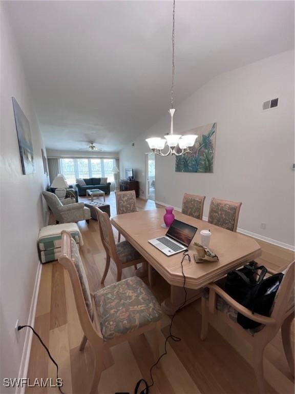 dining area featuring lofted ceiling, ceiling fan with notable chandelier, wood finished floors, visible vents, and baseboards