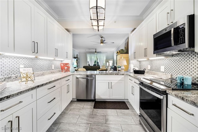 kitchen with kitchen peninsula, appliances with stainless steel finishes, sink, decorative light fixtures, and white cabinetry