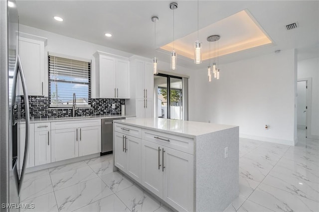 kitchen featuring appliances with stainless steel finishes, a tray ceiling, decorative light fixtures, white cabinets, and a center island