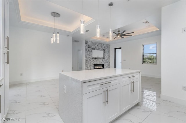 kitchen with a raised ceiling, a stone fireplace, white cabinetry, and hanging light fixtures