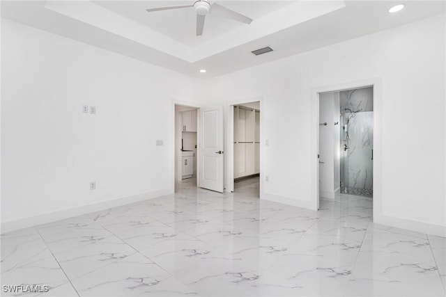 unfurnished bedroom with ensuite bath, ceiling fan, a raised ceiling, a walk in closet, and a closet