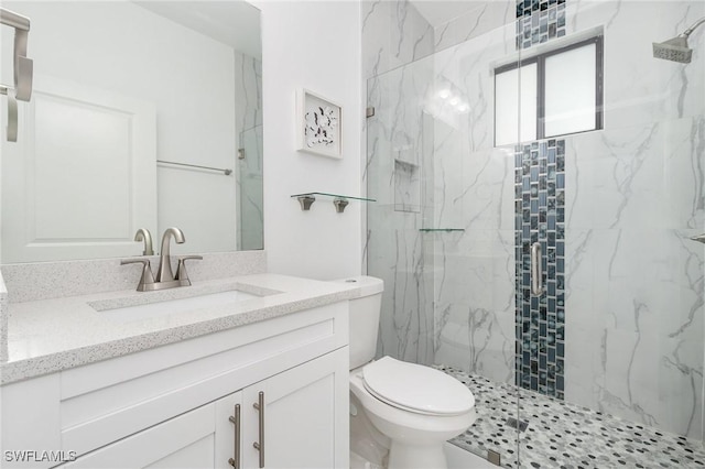 bathroom featuring a shower with door, vanity, and toilet