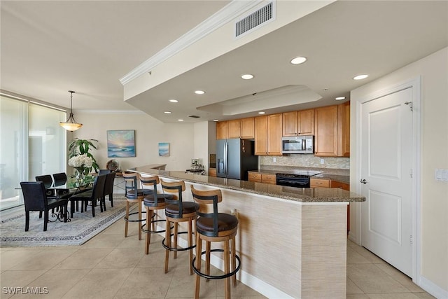 kitchen featuring dark stone counters, a breakfast bar area, ornamental molding, decorative light fixtures, and stainless steel appliances