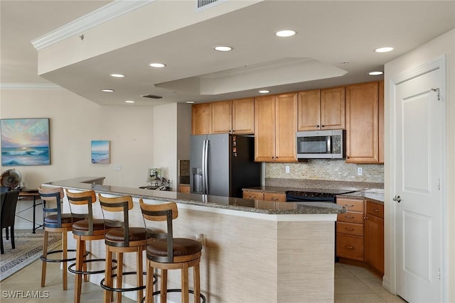 kitchen featuring stainless steel appliances, a tray ceiling, a breakfast bar, light tile patterned flooring, and ornamental molding