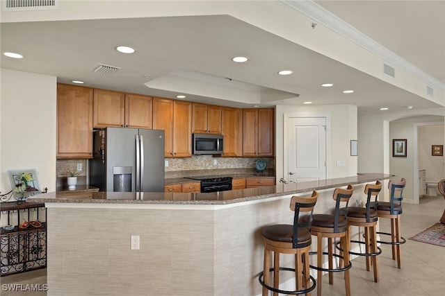 kitchen with kitchen peninsula, appliances with stainless steel finishes, a kitchen bar, and decorative backsplash