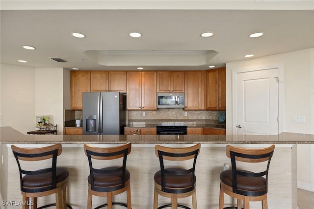 kitchen with a kitchen bar, a raised ceiling, tasteful backsplash, and stainless steel appliances