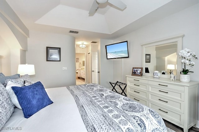 bedroom featuring ensuite bath, a raised ceiling, and ceiling fan