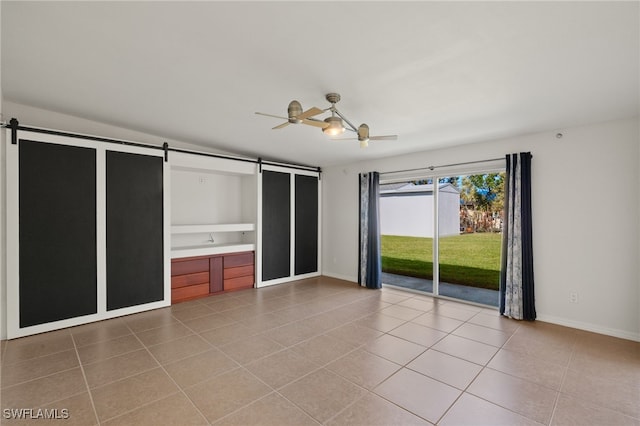 unfurnished bedroom featuring access to outside, connected bathroom, ceiling fan, tile patterned floors, and a barn door