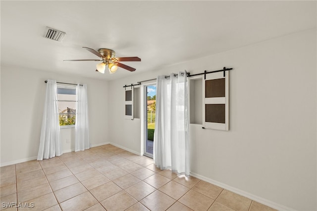 empty room featuring ceiling fan, light tile patterned floors, and a barn door