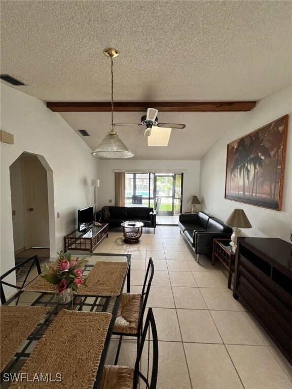 tiled dining space featuring ceiling fan, a textured ceiling, and lofted ceiling with beams