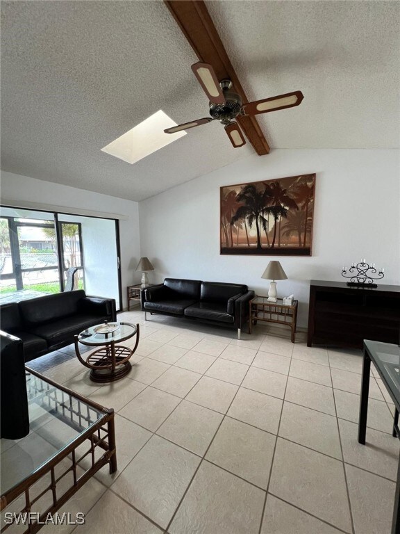 tiled living room featuring ceiling fan, vaulted ceiling with skylight, and a textured ceiling