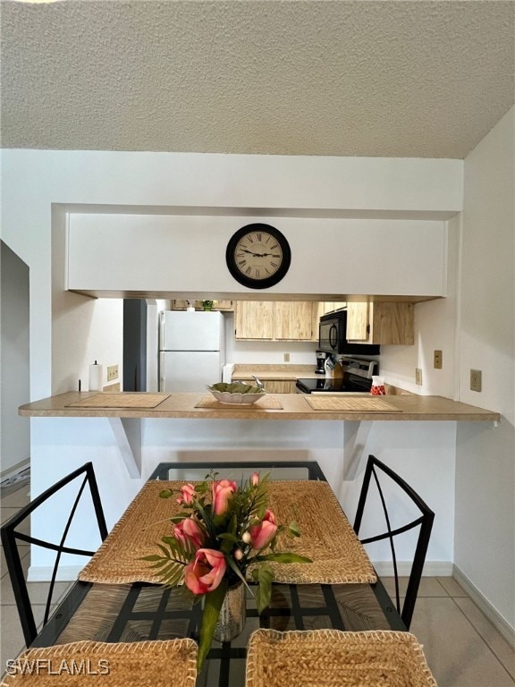 kitchen featuring white fridge, kitchen peninsula, a kitchen breakfast bar, a textured ceiling, and light tile patterned floors