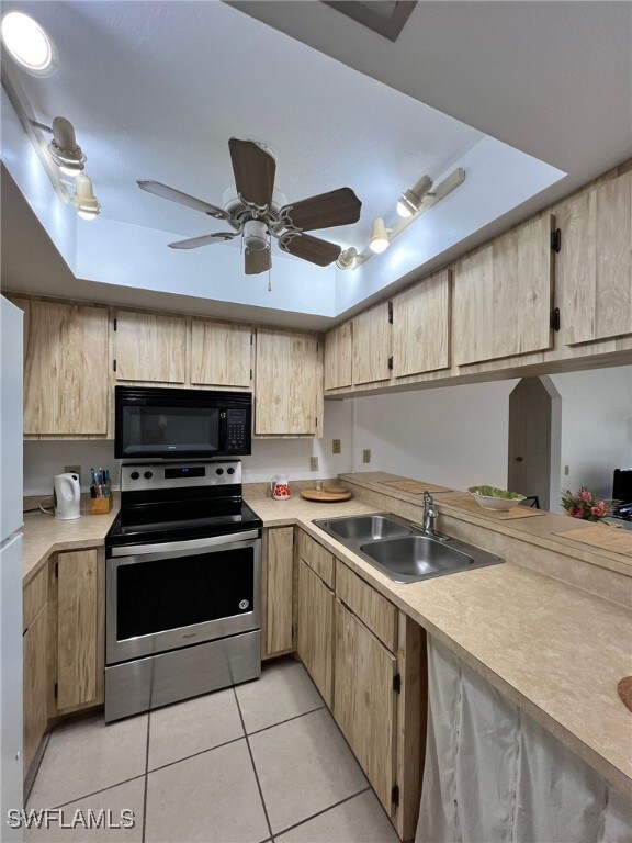 kitchen with stainless steel range with electric stovetop, light tile patterned floors, a raised ceiling, light brown cabinetry, and sink