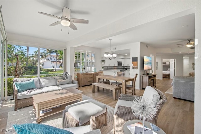 living room featuring ceiling fan with notable chandelier and light hardwood / wood-style flooring