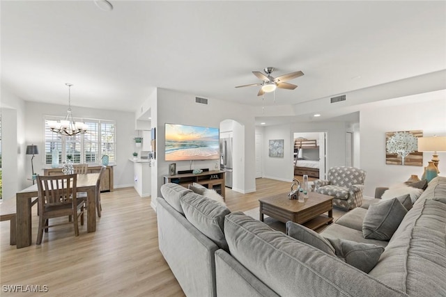 living room with ceiling fan with notable chandelier and light hardwood / wood-style flooring