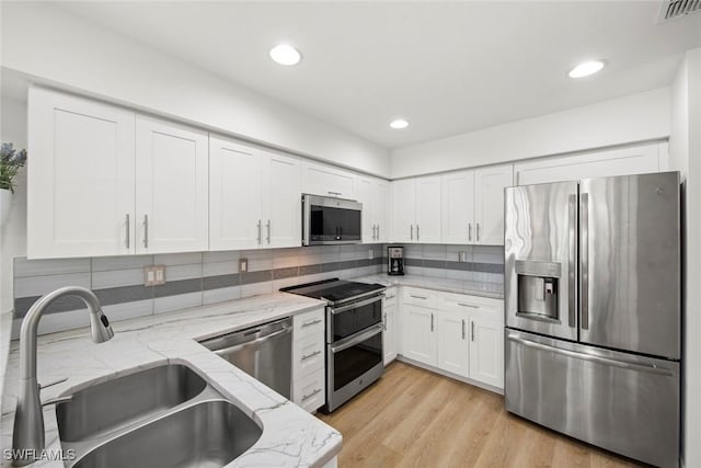 kitchen with light stone countertops, appliances with stainless steel finishes, tasteful backsplash, white cabinetry, and sink