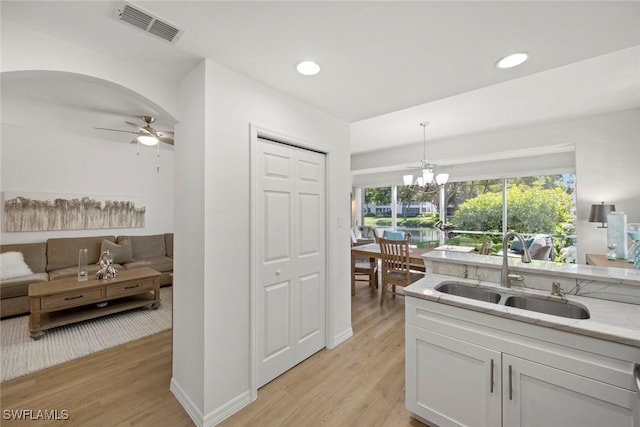 kitchen featuring light hardwood / wood-style floors, hanging light fixtures, sink, white cabinets, and ceiling fan with notable chandelier