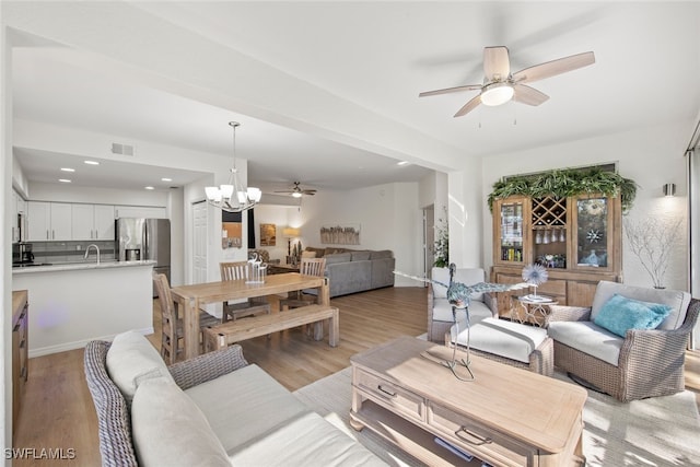 living room featuring ceiling fan with notable chandelier and light hardwood / wood-style flooring