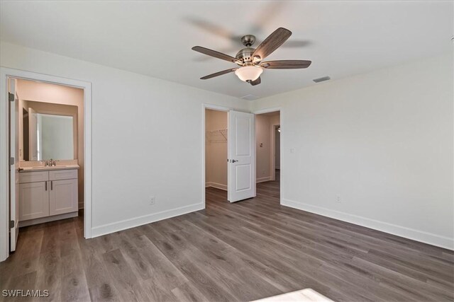 unfurnished bedroom with a spacious closet, wood finished floors, baseboards, and a sink